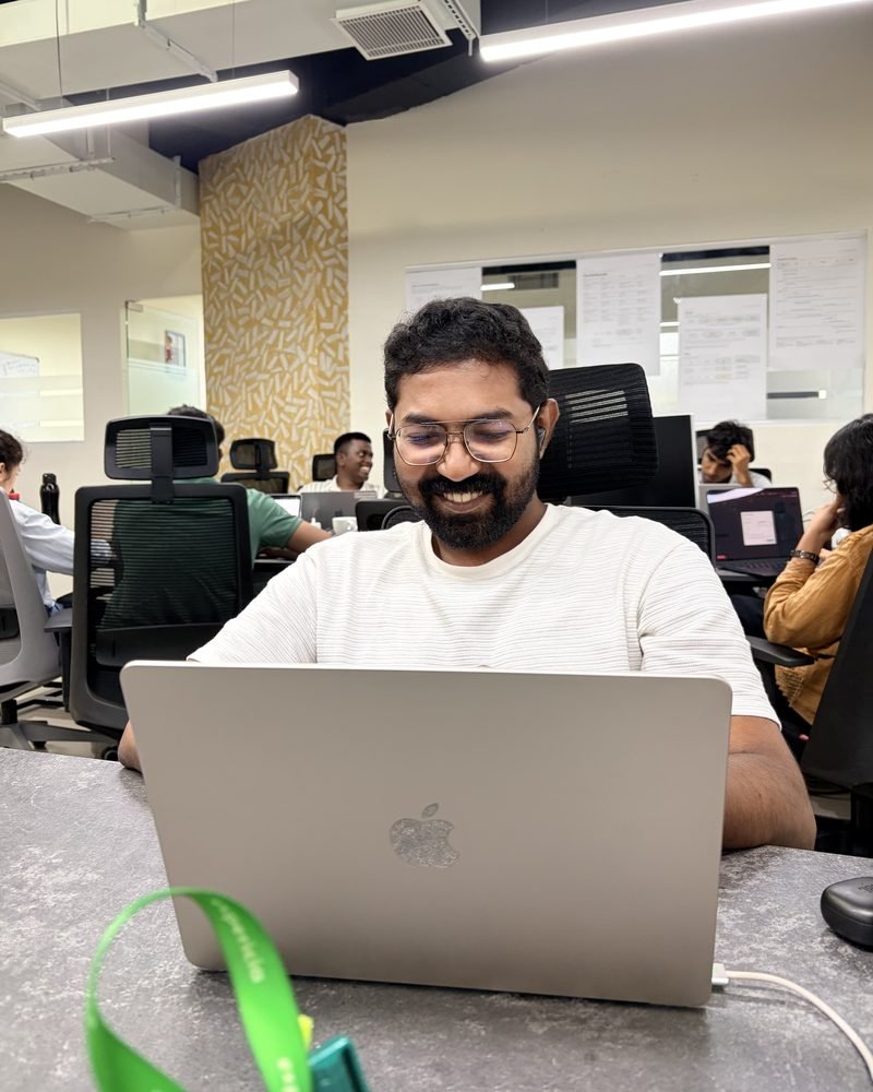 An Expericia engineer at work on his laptop, the rest of the team behind him at the Kochi office