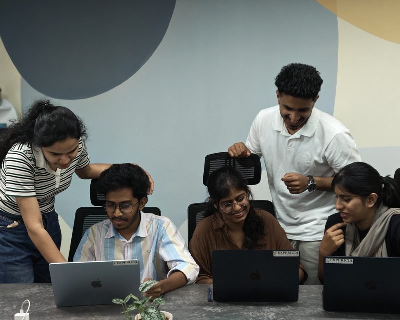 The Expericia team gathered around laptops at the Kochi office, reviewing work together